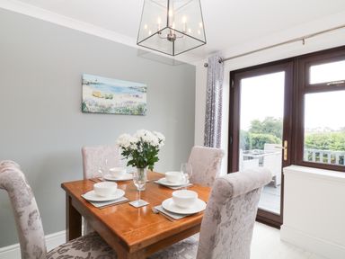 A dining room with a wooden table set for four and floral chairs by glass doors at 12 Claremont Falls Polperro