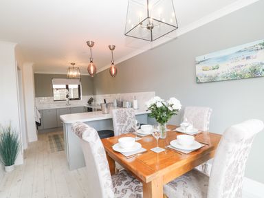 A dining area with a wooden table set for four and a kitchen with grey cabinets in the background at 12 Claremont Falls in Polperro