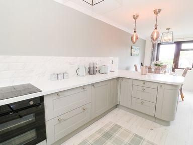 A kitchen with light gray cabinets white countertop and three pendant lights at 12 Claremont Falls in Polperro