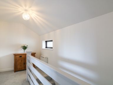 A hallway with a wooden cabinet and flowers on top near a small window at 12 Claremont Falls in Polperro