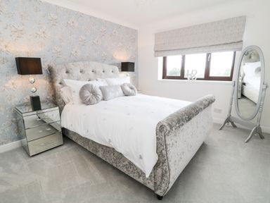 A bedroom with a bed with cushions bedside tables lamps a full length mirror and a window at 12 Claremont Falls in Polperro