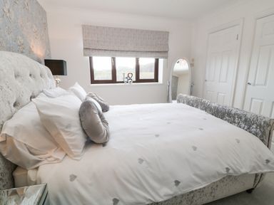 A bedroom with a bed white bedding pillows a full length mirror and a window with blinds at 12 Claremont Falls in Polperro