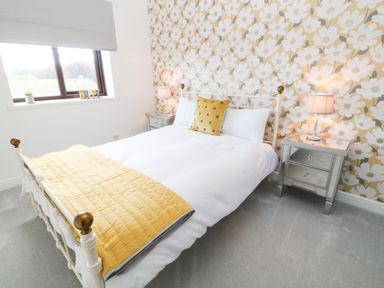 A bedroom with a bed with white linens yellow pillow and quilt two bedside tables with lamps and floral wallpaper at 12 Claremont Falls Polperro