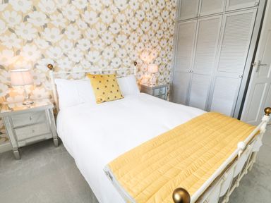 A bedroom with a bed yellow and white bedding bedside tables with lamps and floral wallpaper at 12 Claremont Falls in Polperro