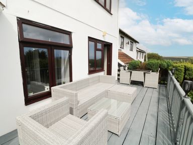 A balcony with white wicker furniture including a sofa armchair and glass top table at 12 Claremont Falls in Polperro