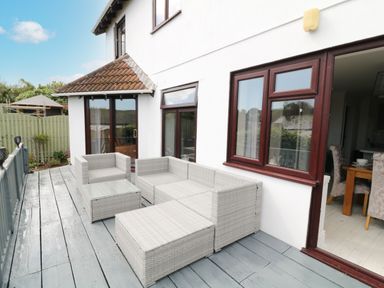 An outdoor deck with gray wicker furniture including a sectional sofa armchair and coffee table attached to a white house at 12 Claremont Falls in Polperro