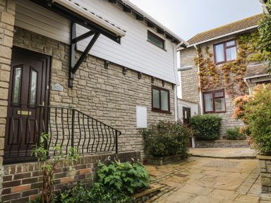 An exterior view of stone houses with plants and a paved walkway at 12 Claremont Falls in Polperro