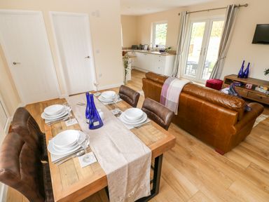 A dining area with a wooden table set for four and a leather sofa in a living room with kitchen in background at Ramsey Lodge Bier Wood Lodges Manorbier