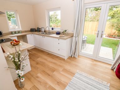 A kitchen with white cabinets wooden countertops a sink a toaster kettle and glass doors to a garden at Ramsey Lodge Bier Wood Lodges in Manorbier