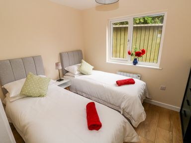 A bedroom with two single beds with gray headboards and red towels on white bedding at Ramsey Lodge Bier Wood Lodges in Manorbier