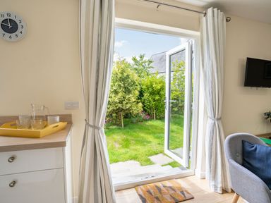A room with an open door leading to a garden with trees and bushes at Ramsey Lodge Bier Wood Lodges in Manorbier