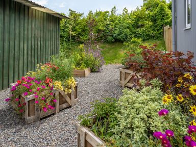 A garden area with wooden planter boxes filled with colorful flowers and plants on a gravel path at Ramsey Lodge in Manorbier
