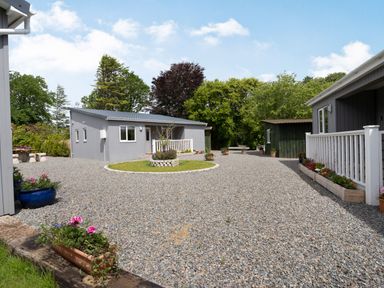A gravel driveway with planters and small buildings surrounded by trees at Ramsey Lodge Bier Wood Lodges in Manorbier