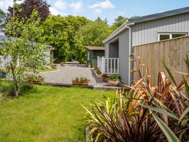 A gravel pathway with potted plants and green trees beside gray buildings with white railings at Ramsey Lodge Bier Wood Lodges in Manorbier