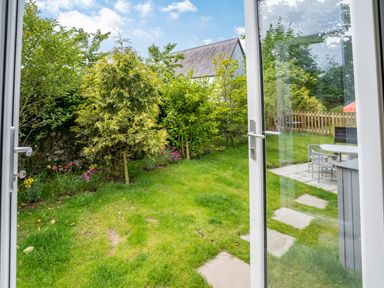 A garden with grass trees flowers and a patio with chairs and table at Ramsey Lodge Bier Wood Lodges in Manorbier