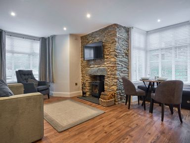 A living room with a stone fireplace and a wall-mounted TV next to a round dining table with chairs at Lower Sheriff's Place in Windermere