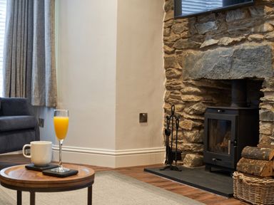 A living room with a stone fireplace wood burner a glass of orange juice and a mug on a table at Lower Sheriff's Place in Windermere