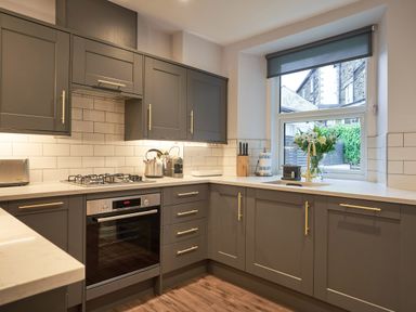 A kitchen with grey cabinets a gas stove oven kettle coffee machine knife block flowers in a vase by the window at Lower Sheriff's Place in Windermere
