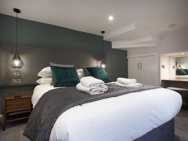 A bedroom with a large bed with pillows and towels bedside tables and hanging lamps at Lower Sheriffs Place in Windermere