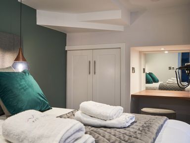 A bedroom with a bed with green pillows towels on the bed a pendant light and a dressing table at Lower Sheriff's Place in Windermere