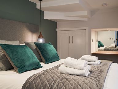A bedroom with a bed with green and gray pillows folded towels on a quilted bedspread and a white cabinet at Lower Sheriff's Place in Windermere