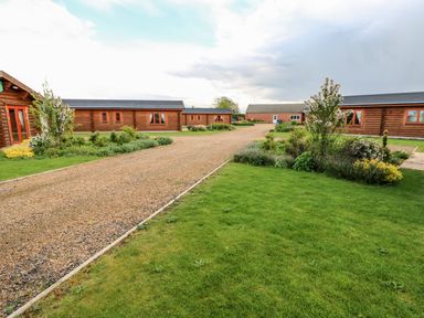 A gravel pathway with green lawns and shrubs bordered by wooden lodges at Oak Lodge in Greetham Rutland