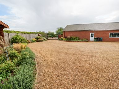 An outdoor area with gravel ground a red brick building plants along a wooden fence and a metal gate at Oak Lodge in Greetham Rutland