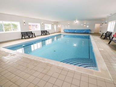 An indoor swimming pool with tiled floor benches along the walls and windows at Oak Lodge in Greetham Rutland