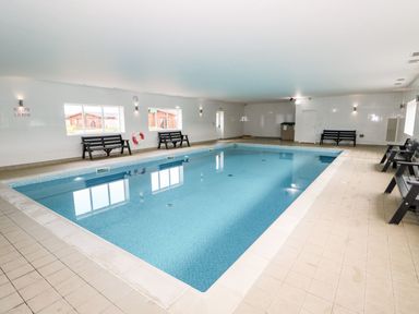 An indoor swimming pool with benches along the walls at Oak Lodge in Greetham Rutland