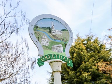 A village sign with illustrations of buildings and a river at Greetham in Rutland