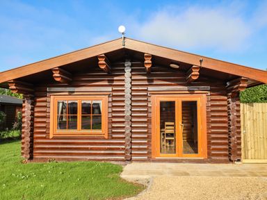 A log cabin with wooden framed window and glass double doors on grass and gravel at Oak Lodge in Greetham Rutland
