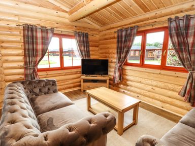 A living room with two sofas a wooden coffee table a TV on a stand and windows with patterned curtains at Oak Lodge in Greetham Rutland