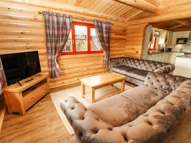 A living room with tufted sofas, wooden coffee table, television on wooden stand, and window with plaid curtains at Oak Lodge in Greetham Rutland