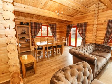 A wooden dining table with six chairs next to a bookshelf and two brown sofas in a wooden log cabin at Oak Lodge in Greetham Rutland