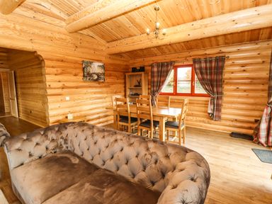 A room with a brown couch and wooden dining table with chairs near window with curtains at Oak Lodge in Greetham Rutland