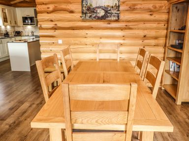 A dining area with a wooden table and six wooden chairs next to a kitchen in Oak Lodge Greetham Rutland