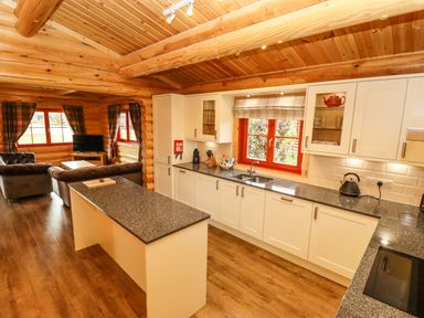 A kitchen with white cabinets and a countertop island adjacent to a living area with sofas and a television at Oak Lodge in Greetham Rutland