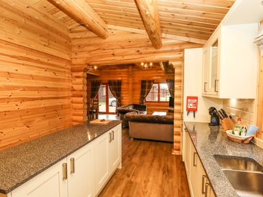 A kitchen with white cabinets and granite countertops opening to a living room with gray sofas and plaid curtains at Oak Lodge in Greetham Rutland