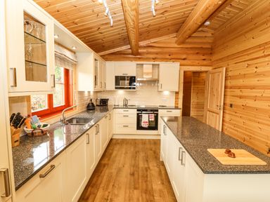 A kitchen with white cabinets granite countertops wooden walls and ceiling and a wooden floor at Oak Lodge in Greetham Rutland