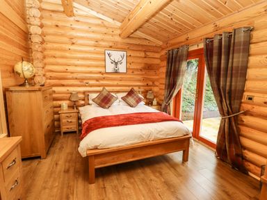 A bedroom with a wooden bed framed by log cabin walls and plaid curtains at Oak Lodge in Greetham Rutland