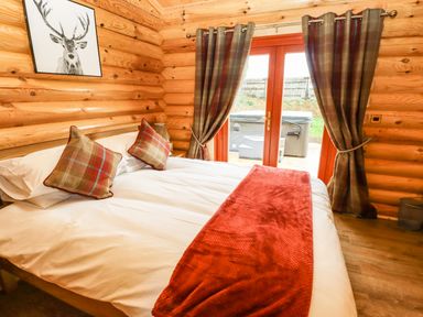 A bedroom with a bed with pillows and a red blanket near glass doors with curtains at Oak Lodge in Greetham Rutland
