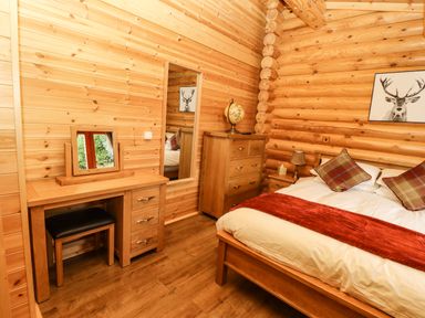 A bedroom with a wooden bed covered with white and red linens a wooden dresser a vanity table with a mirror and stool and a framed deer picture on the wall at Oak Lodge in Greetham Rutland