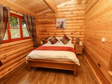 A bedroom with a double bed with cushions and a runner between two bedside tables with lamps and a window with curtains at Oak Lodge in Greetham Rutland