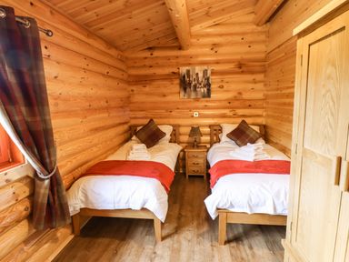 A bedroom with two single beds a nightstand a lamp and a wardrobe in a wooden cabin at Oak Lodge in Greetham Rutland