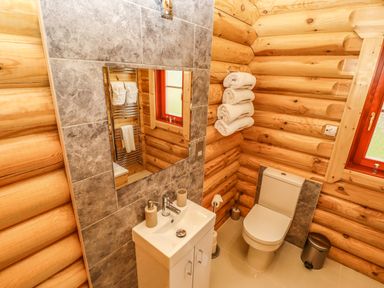 A bathroom with a sink cabinet mirror toilet rolled towels on a rack and a window at Oak Lodge Greetham Rutland