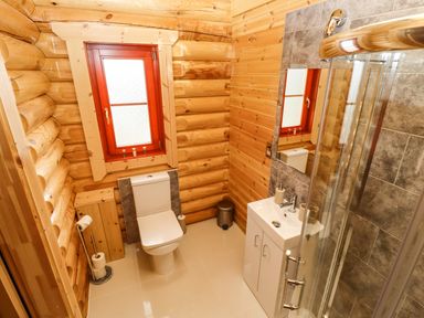 A bathroom with a toilet sink shower window and wooden walls at Oak Lodge in Greetham Rutland