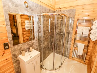 A bathroom with a glass shower enclosure a white sink with cabinet a mirror and a towel rack at Oak Lodge in Greetham Rutland