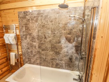 A bathroom with a bathtub shower and towels on a rack at Oak Lodge in Greetham Rutland