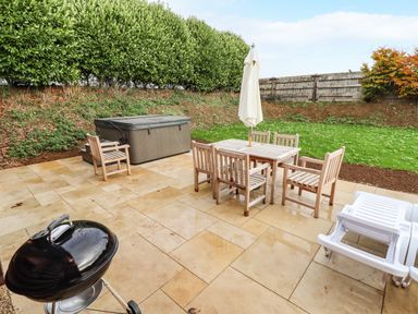An outdoor patio area with a wooden table and chairs with an umbrella a closed hot tub a barbecue grill and plastic lounge chairs at Oak Lodge in Greetham Rutland