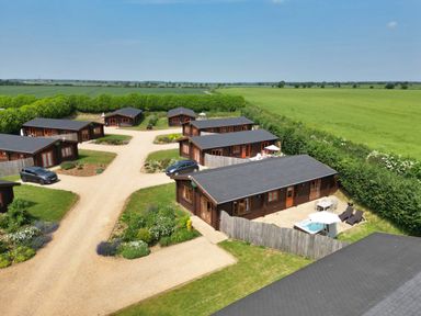 An aerial view of a cluster of wooden lodges with driveways and parked cars surrounded by green fields at Oak Lodge in Greetham Rutland